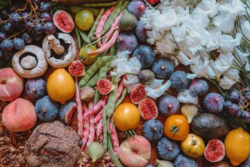 A colorful assortment of fresh fruits, vegetables, bread, and flowers arranged beautifully on a wooden table.