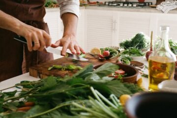 Adult preparing a fresh vegetable salad in a cozy kitchen with various ingredients and kitchenware.