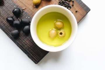 Top view of green olives in oil, black olives, and pepper on a cutting board.